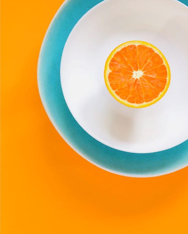 Orange cut in half in a blue and white plate on an orange table